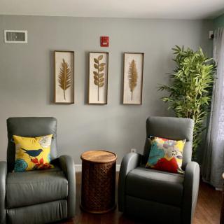 A cozy living room with two chairs, decorative pillows, wall art, and a potted plant.