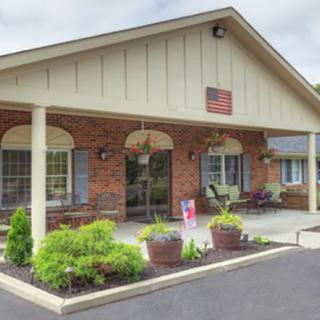 A welcoming brick building entrance with a porch and landscaped greenery.
