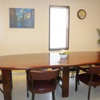 A conference room with a large table, several chairs, artwork on the wall, and a clock.
