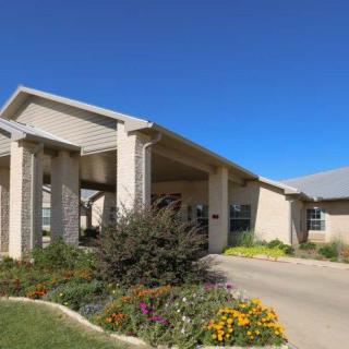 A modern building with a covered entrance, surrounded by landscaped gardens and a driveway.