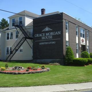 A two-story building with a large sign on the side, surrounded by a well-maintained lawn and garden.