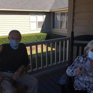 Two people wearing masks sitting on a porch.