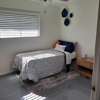 A cozy minimalist bedroom with a single bed, decorative pillows, and a nightstand under window blinds.