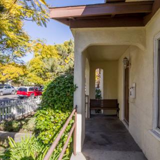 A sunny porch with a view of trees and parked cars.