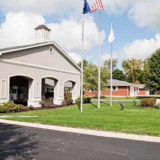 A building with three flag poles surrounded by a lawn and trees under a partly cloudy sky.