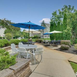 A peaceful outdoor patio area with tables, chairs, and umbrellas surrounded by lush greenery and a well-maintained pathway.