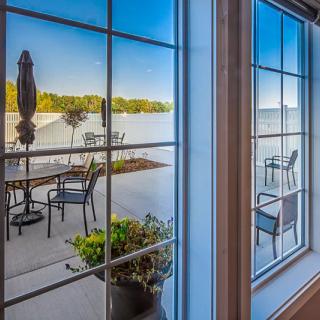 A scenic view of a patio overlooking a peaceful lake, as seen through a large window.