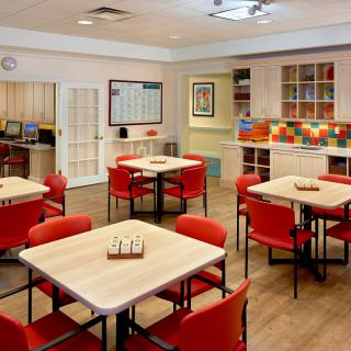 A brightly colored community dining area featuring red chairs and decorative tile accents.