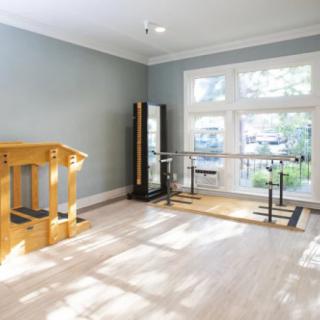 A well-lit home gym featuring a barre, mirrors, and light wood flooring.