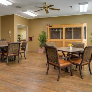 A neatly arranged dining area with multiple tables and chairs, featuring a ceiling fan and warm lighting.