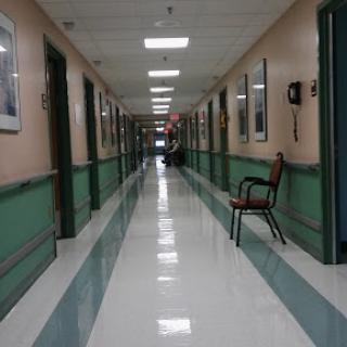 A quiet corridor in a hospital, featuring green and beige walls with photographs and a solitary chair.