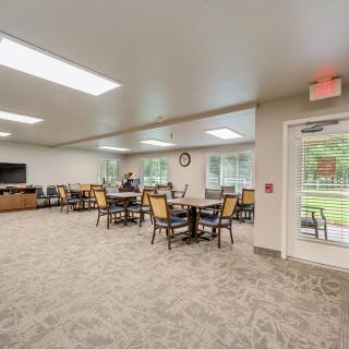 A spacious dining area with several tables and chairs, featuring a television and large windows.