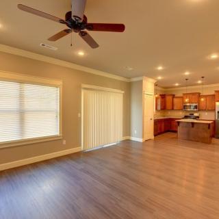 A spacious open floor plan living room leading into a kitchen with hardwood flooring and modern amenities.