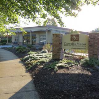 A view of a building surrounded by landscaping with a prominent sign and sidewalk under sunny conditions.