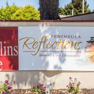 Sign for Peninsula Reflections, a senior living community, surrounded by a garden.