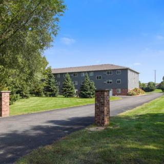 A building with a paved driveway surrounded by lush greenery and trees under a clear blue sky.