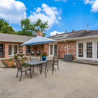 A spacious backyard patio featuring outdoor furniture and an umbrella, set against a brick house under a clear blue sky.