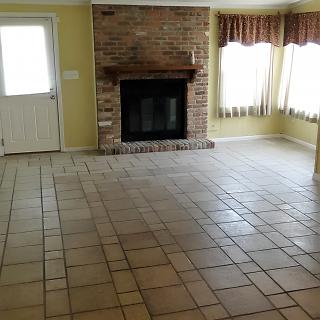 An empty living room with a brick fireplace and tile flooring.