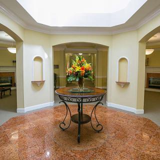 A beautifully decorated lobby features a central table with a vibrant flower arrangement, surrounded by elegant architecture.