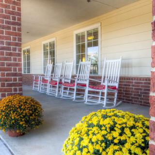 A cozy porch with white rocking chairs and vibrant yellow flowers in pots.
