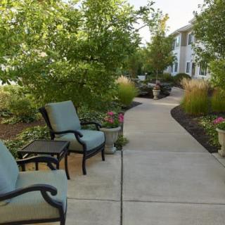 A serene garden pathway with outdoor chairs surrounded by lush greenery.