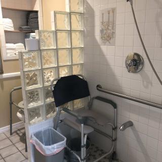 An accessible bathroom featuring a shower with a chair and handrails.