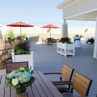 A sunny beachside patio with tables, chairs, and red umbrellas.