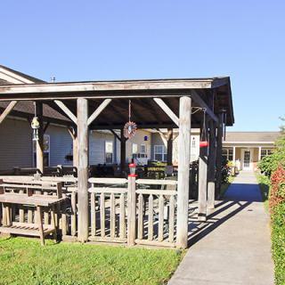 A sunlit patio with wooden structures and furniture leads to a building.