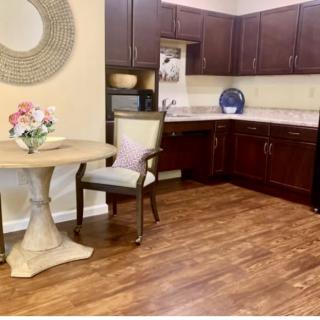 A cozy kitchen with wooden flooring, featuring dark cabinets and a small dining area with a table and chair.