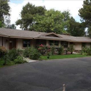 A ranch-style residential house surrounded by trees, with a driveway in front.