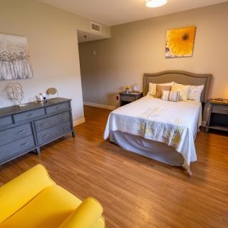 A cozy bedroom with a bed, gray dresser, and a bright yellow chair.