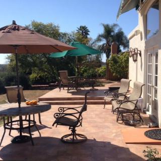A sunny patio with outdoor furniture and umbrellas, surrounded by greenery.