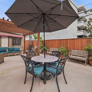 A cozy outdoor patio features a table with an umbrella, surrounded by comfortable seating and greenery.