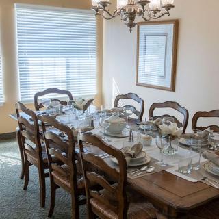 A formal dining room set up with a table prepared for a meal, featuring elegant tableware and a chandelier above.