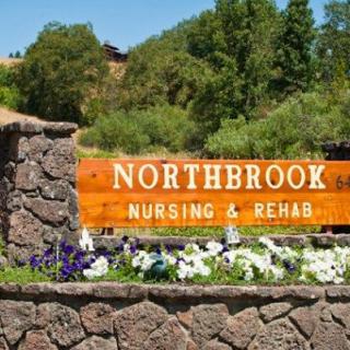Sign for Northbrook Nursing & Rehab surrounded by greenery and flowers.