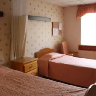 A hospital room with two patient beds and wooden furniture.