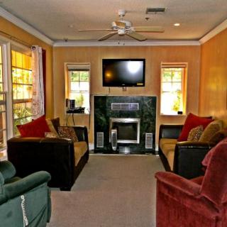 A cozy living room with comfortable seating, a television mounted above a fireplace, and natural light from the windows.