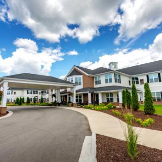 A modern residential building with a landscaped driveway under a partly cloudy sky.