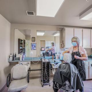 A hairdresser wearing a mask styles a client's hair in a salon.