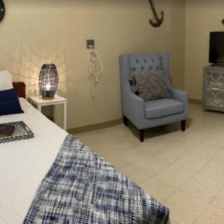 A cozy bedroom featuring a tufted armchair, a neatly made bed with a patterned blanket, and a television on a dresser.