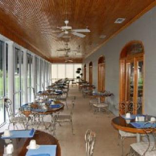 A spacious restaurant dining area with glass windows, wooden ceiling, and neatly arranged tables and chairs.