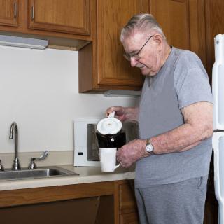 An older adult preparing coffee in a kitchen.