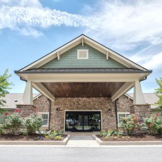 A front view of a building entrance with a covered entryway and landscaped surroundings under a partly cloudy sky.