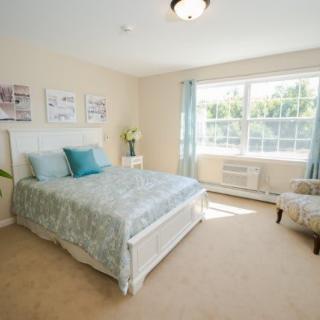 A bright and airy bedroom with a neatly made bed, large window, and tasteful decor.
