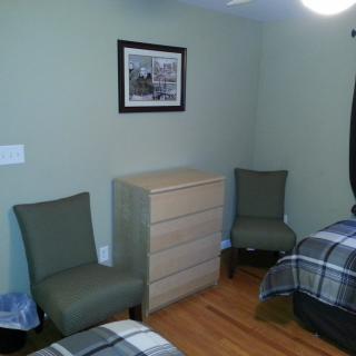 A neatly arranged bedroom with two beds, chairs, and a dresser.