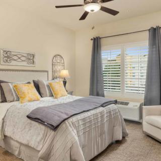 A cozy bedroom with a large bed, decorative pillows, curtains, and a ceiling fan.