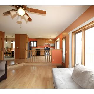 A spacious open floor plan featuring a living area with wood flooring, connecting seamlessly to the kitchen, all flooded with natural light from large windows.