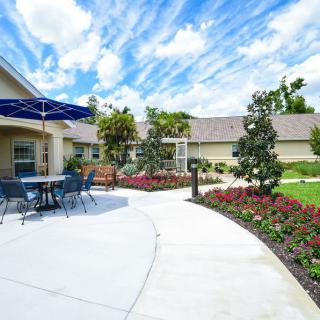 A sunny garden patio with a pathway, surrounded by vibrant flowers and outdoor seating.