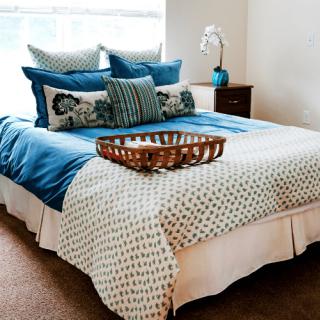 A neatly made bed in a cozy bedroom, featuring blue and white bedding with decorative pillows and a wicker basket on top.