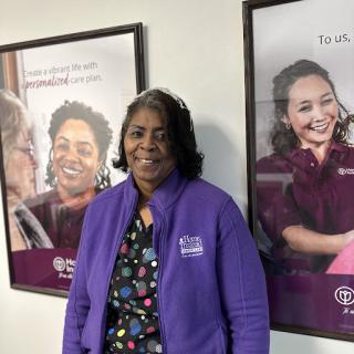 A joyful moment captured indoors with a person wearing a purple jacket, surrounded by posters of smiling women.